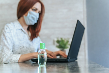 Woman using Laptop with work from home. Sanitizer gel, face mask, and alcohol spray for prevention Coronavirus disease (COVID-19). Healthcare disinfection concept. Selective focus