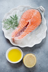 White shell-shaped plate with raw iced salmon steak and seasonings, vertical shot on a light-blue stone background