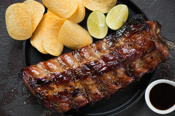Above view of bbq pork ribs glazed in honey and soy sauce and served with potato chips, studio shot