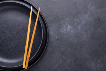 Set of dark plates and chopsticks on stone background. Set for Asian, Japanese and Chinese food. Top view. Copy space
