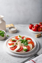 Italian caprese salad with sliced tomatoes, mozzarella, basil, olive oil on a light background, place for text.