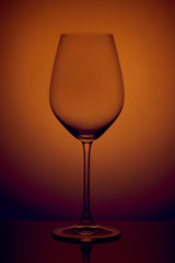 The crystal glass stands on the reflecting surface on a orange background. studio photo. product. Beautiful shadow from wine glass. macro photo