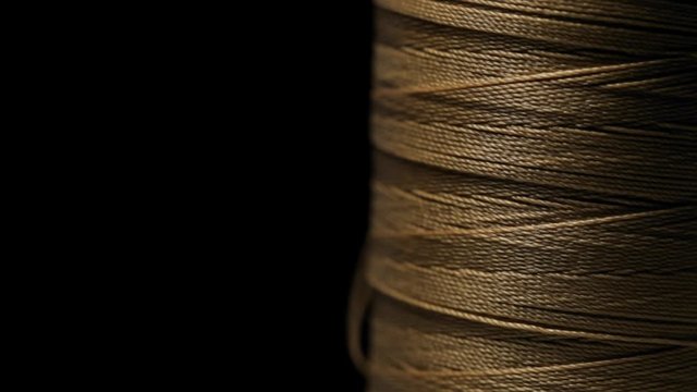 The spool with beige threads unwinds rotates on a black background close up