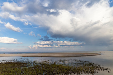 Sandy beach by the sea on a sunny day with white cumulus and feather clouds in the sky.