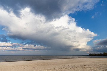 Sandy beach by the sea on a sunny day with white cumulus and feather clouds in the sky.