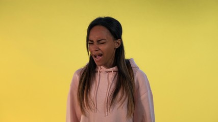 Good-looking african girl screaming loudly. There is yellow background.