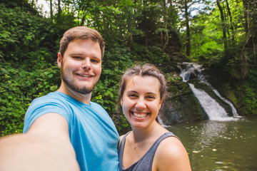 smiling couple taking selfie in front of waterfall in woods