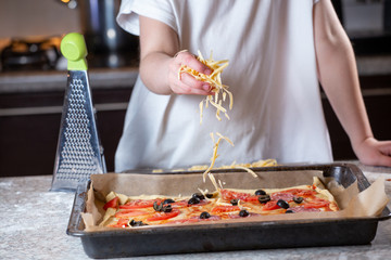Girl sprinkles cheese on pizza