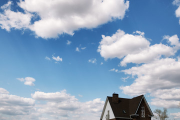 House roof under blue sky with white clouds. Cloudscape. Brown Roof with chimney. White cumulus clouds high sky over roof.