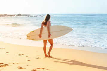 Naklejka na ściany i meble Beautiful sexy surfer girl standing on the beach with surf desk.