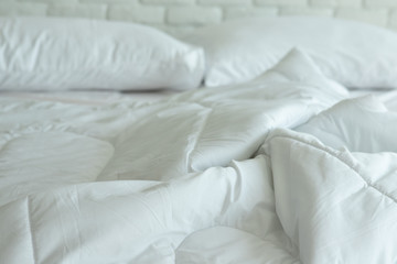 Messed bed with white pillow and blanket with natural light in bedroom in the morning,