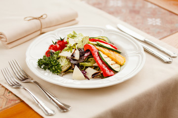 grilled vegetables with cheese and herbs, seasoned with balsamic vinegar. served on a white round plate on a style covered with a beige tablecloth
