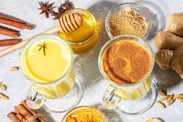 Organic turmeric milk. Two glasses for mulled wine with golden milk with ingredients on light grey backdrop with shadows. Alternative medicine. Healthy eating and detox. Selective focus, close up.