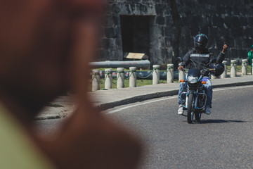 Motorcycle taxi in Cartagena, Colombia. Motorbike driver waving to a customer with an extra helmet on his elbow, ready for the passenger.