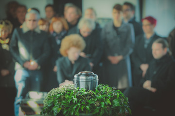 A metal urn with ashes of a dead person on a funeral, with people mourning in the background on a...