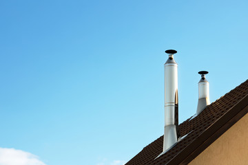 Two modern style chimneys from oven and fireplace stacked stainless steel on tiled roof made...