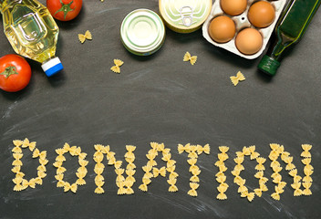 Food donations on black background, top view, copy space with word DONATION laid out from pasta