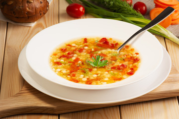 Italian soup with red lentils and small pasta - ptitim. Added vegetables, herbs and spices. In a plate is a spoon. Background raw vegetables, brown bread. Rustic