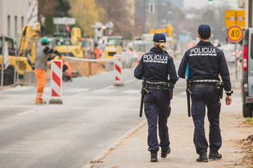 Male and female police officers walking on a pedestrian walkway past the construction zone on a road. Police inspecting work of road maintenance people or workers.