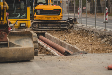 Replacement of pipes or piping under the road surface. Visible pipes under the road bed, surrounded by backhoes or excavators moving earth.