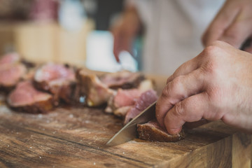 Cutting or slicing beef meat into think chunks or steaks ready to eat. Visible hand with a sharp...