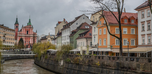 Picturesque buildings along Ljubljanica river on a dull autumn november day. Lazy gray day in Ljubljana, Slovenia, with dirty brown river flowing under the bridge.