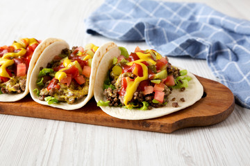 Homemade Cheeseburger Tacos on a rustic wooden board on a white wooden background, side view.