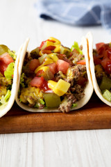 Homemade Cheeseburger Tacos on a rustic wooden board on a white wooden background, side view. Close-up.