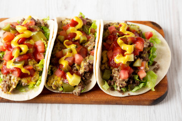 Homemade Cheeseburger Tacos on a rustic wooden board on a white wooden surface, low angle view.