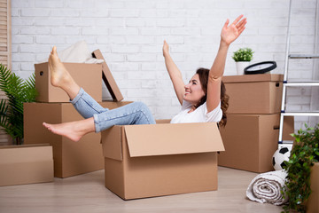 moving day - happy woman sitting in cardboard box in new house