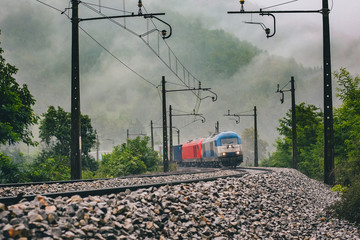 Silver and blue diesel locomotive pulling a freight train in rainy weather on a curve. Goods train on an open track with a silver and red loco.