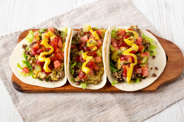 Homemade Cheeseburger Tacos on a rustic wooden board on a white wooden background, side view. Close-up.