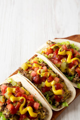 Homemade Cheeseburger Tacos on a rustic wooden board on a white wooden background, low angle view. Copy space.