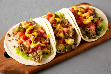 Homemade Cheeseburger Tacos on a rustic wooden board on a gray surface, low angle view. Close-up.