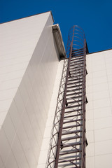 fire metal staircase on a building tiled wall against a blue sky. vertical view