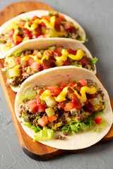 Homemade Cheeseburger Tacos on a rustic wooden board on a gray surface, low angle view.