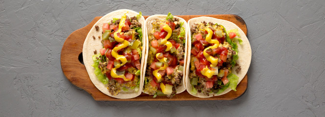 Homemade Cheeseburger Tacos on a rustic wooden board on a gray surface, top view. Flat lay, overhead, from above.
