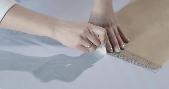 Slow motion video of the fashion designer that works at the table with curves and a pattern, draws a soap slice, around lies scissors, centimeter, a notebook with sketch, sew studio, view from a top