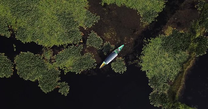 Slow rotating aerial shot with top down view of traditional wooden boat floating on waterway of Dal Lake in Kashmir, India.