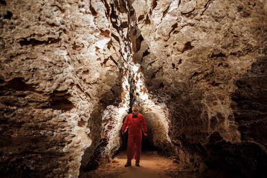Man walking and exploring dark cave with light headlamp underground. Mysterious deep dark, explorer discovering mystery moody tunnel looking on rock wall inside.
