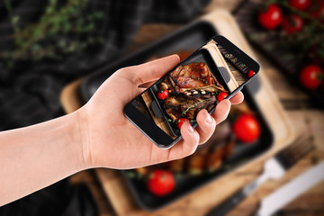 Blogger taking picture of delicious roasted ribs at table, closeup. Food photography