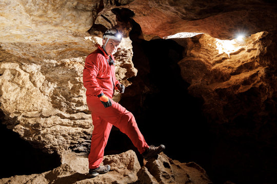 Man walking and exploring dark cave with light headlamp underground. Mysterious deep dark, explorer discovering mystery moody tunnel looking on rock wall inside.