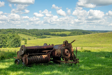 Fototapeta na wymiar Rusty Baler with Rolling Hills in the Background