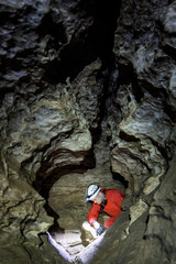 Obraz premium Man walking and exploring dark cave with light headlamp underground. Mysterious deep dark, explorer discovering mystery moody tunnel looking on rock wall inside.