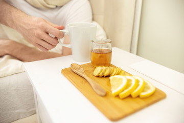 Sick Man in Bed. Man Ill in Bed Self Healing. Self Treatment at Home. Man Drinking Hot Tea in Bed. Honey, Lemon, Ginger and Tea Cup Close Up