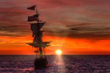 Antique wooden ship leaving the harbor under a bright red sunset spring time