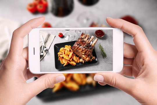 Blogger taking picture of delicious grilled ribs at table, closeup. Food photography