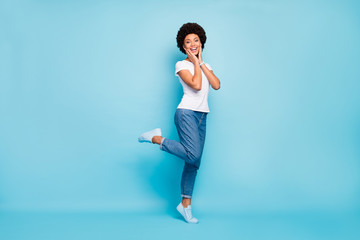 Full body photo of pretty funky dark skin curly lady enjoy sightseeing walk down street sunny summer day tourist traveler wear casual white t-shirt jeans isolated blue color background