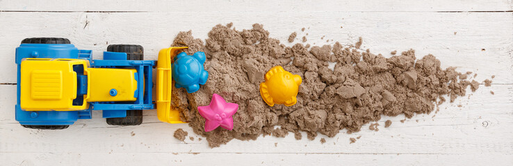 Kinetic sand with colorful molds removes a tractor with a bucket from the table. Top view on...
