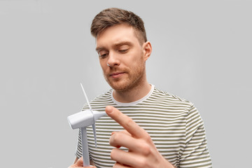 sustainable energy, power and people concept - young man with toy wind turbine over grey background